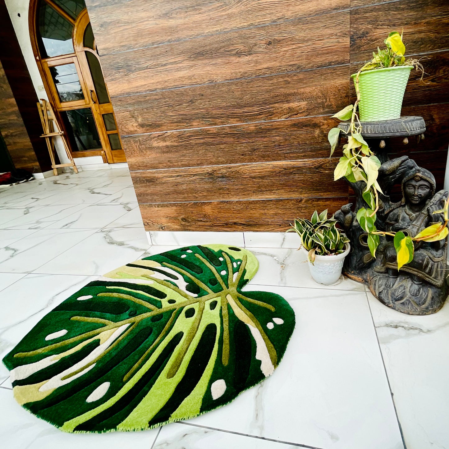 Leaf-shaped hand-tufted rug displaying Monstera plant pattern in natural green shades with organic fenestrations