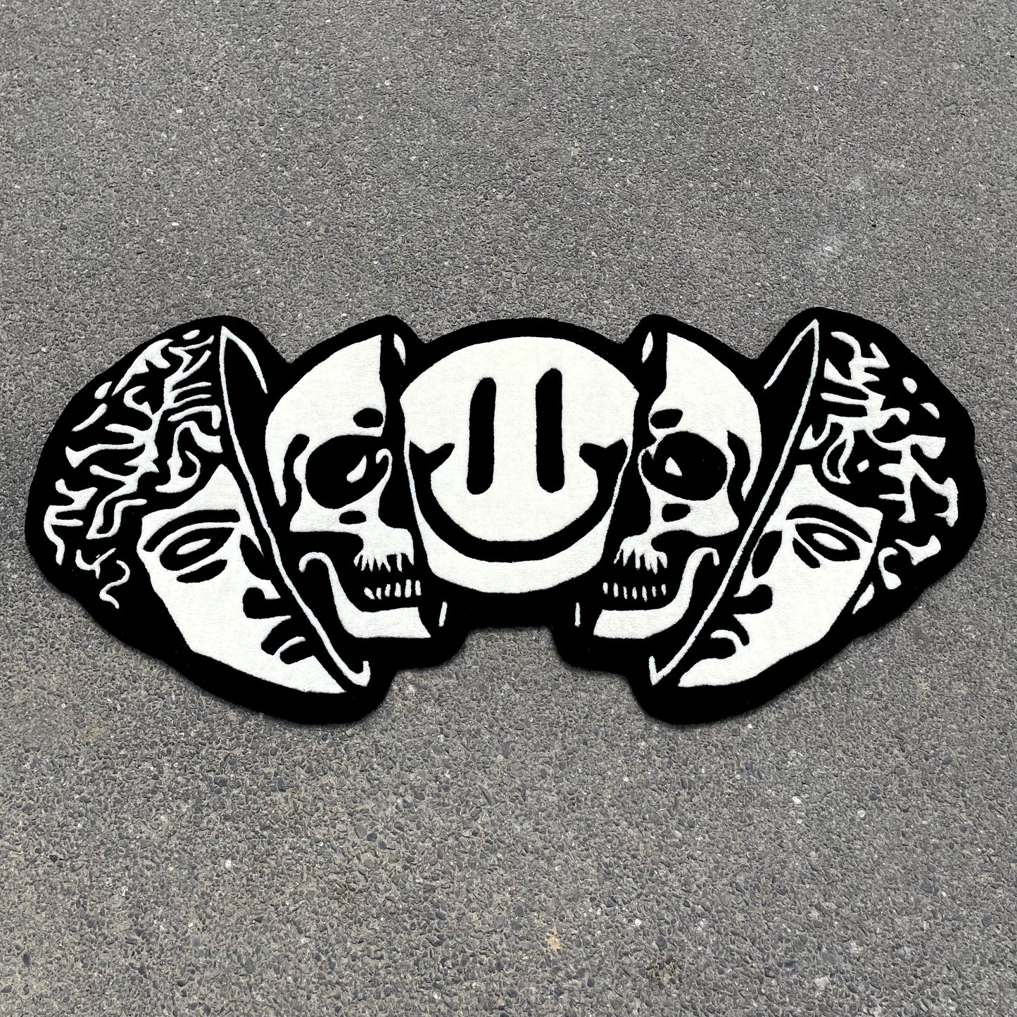 Black and white hand-tufted rug featuring classical Greek head, dual skulls, and smiley face in artistic street art style