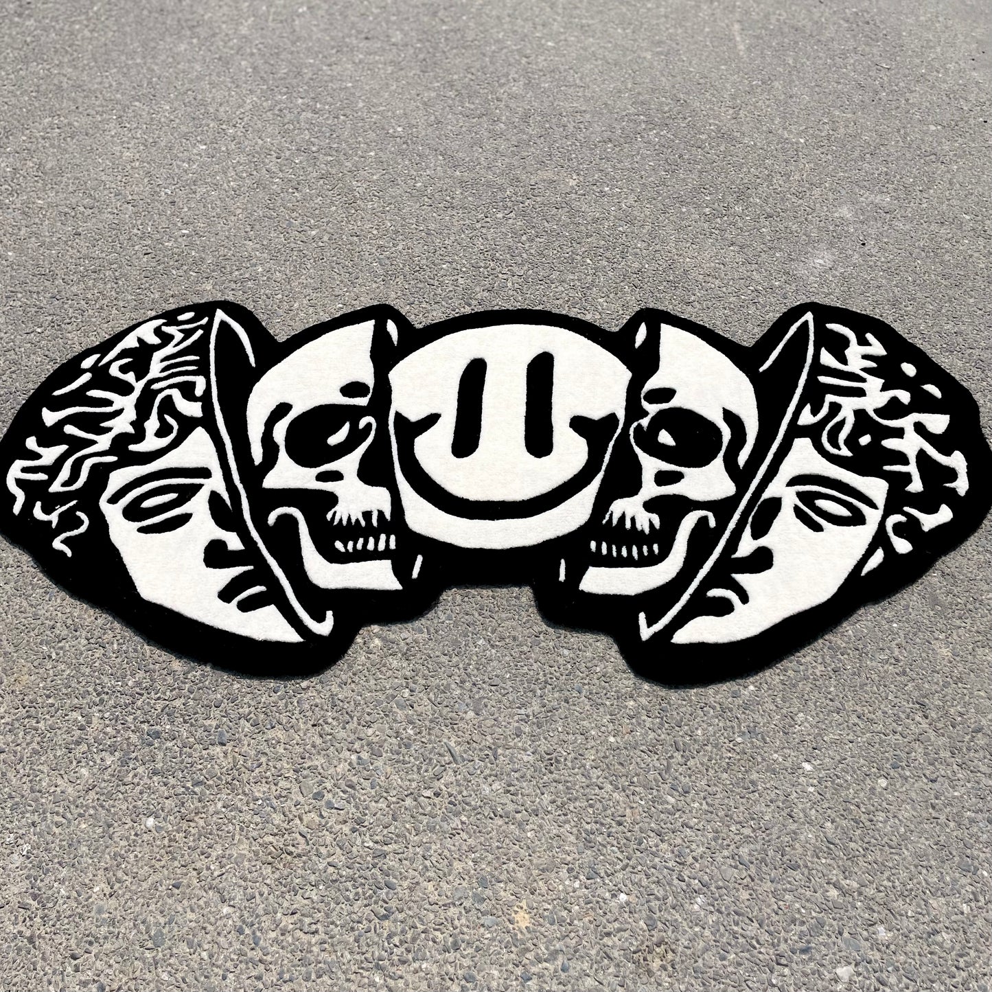 Monochromatic area rug displaying three heads design with Greek statue, skulls, and decorative elements in black and white