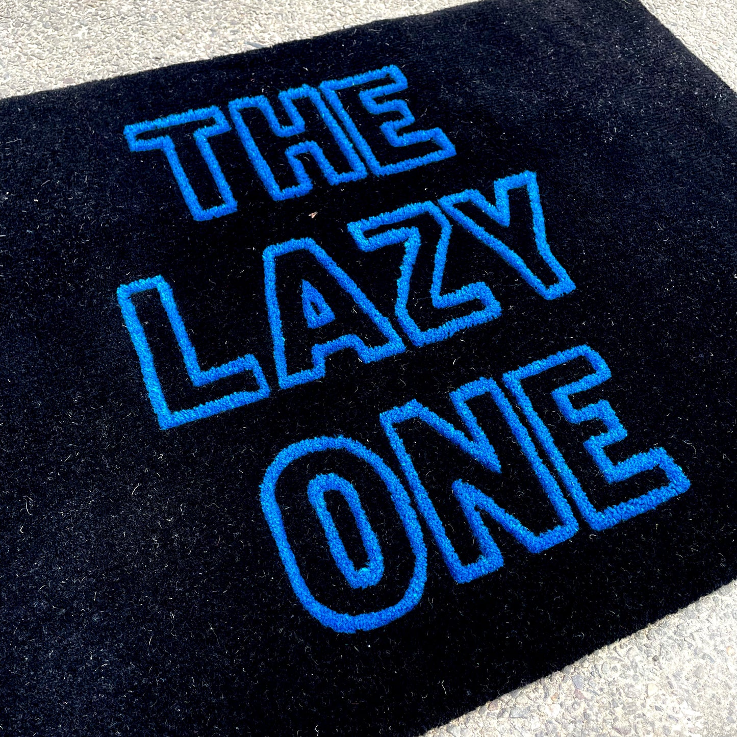 closeup of the lazy one typography custom tufted rug, made in black background and blue font