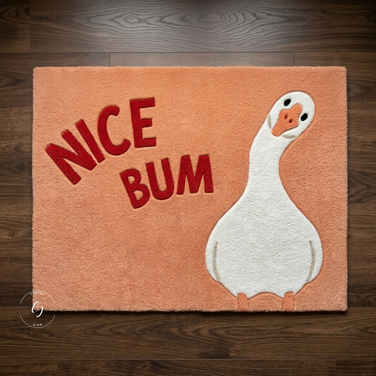 A rectangular peach-colored plush tufted rug featuring the words 'NICE BUM' in red and a white duck illustration on the right, shown laid flat on a dark wood floor.