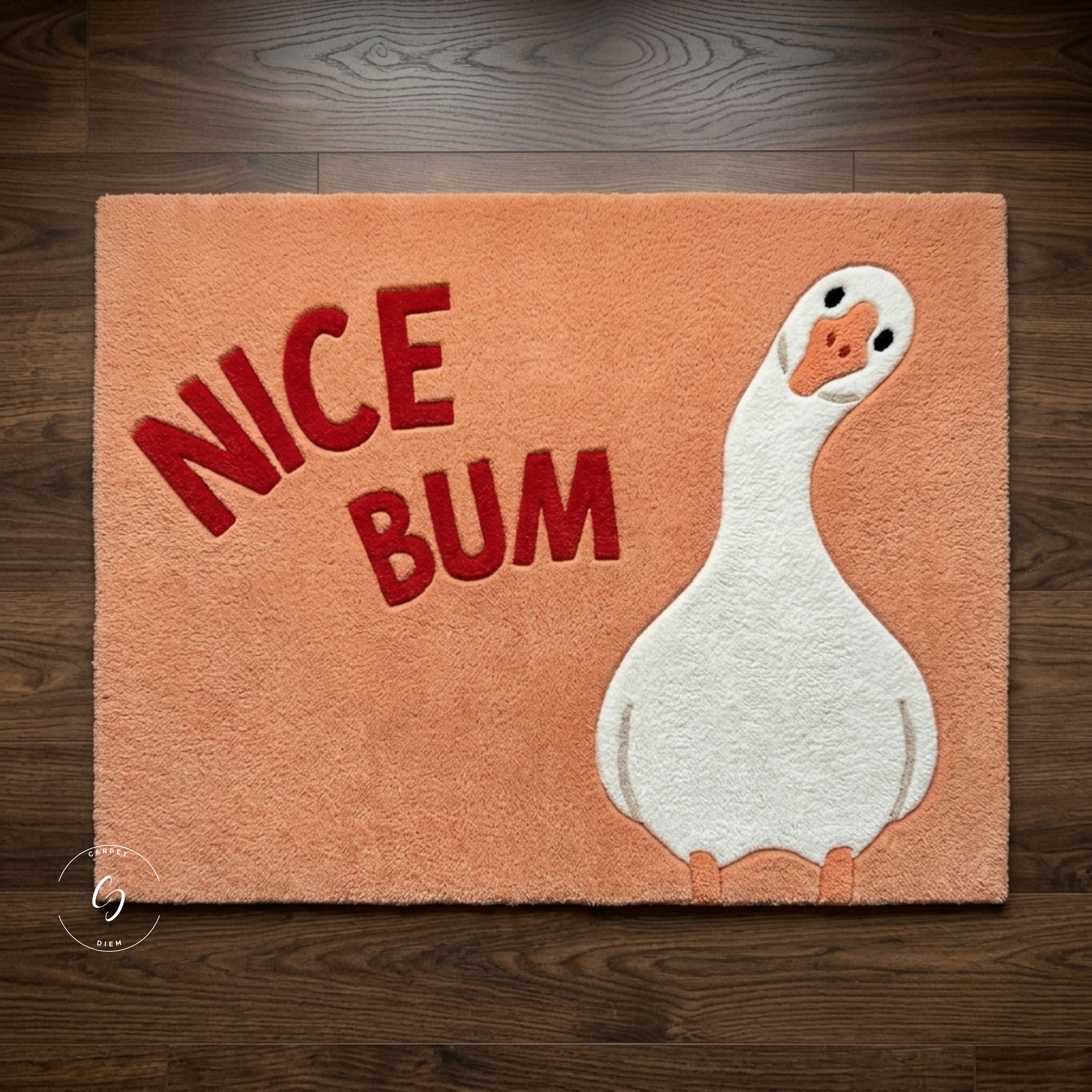 A rectangular peach-colored plush tufted rug featuring the words 'NICE BUM' in red and a white duck illustration on the right, shown laid flat on a dark wood floor.