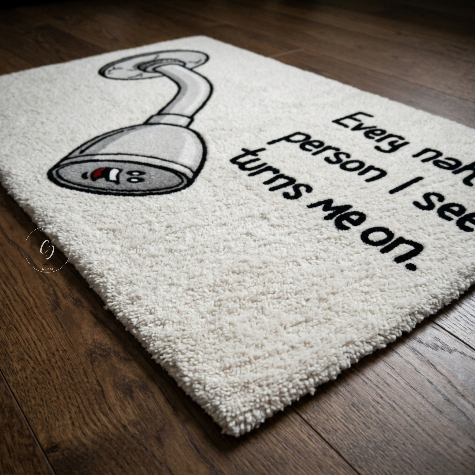 A cream-coloured hand tufted rug with a cartoon shower head and the text 'Every naive person I see turns me on.' placed on a dark wood floor.
