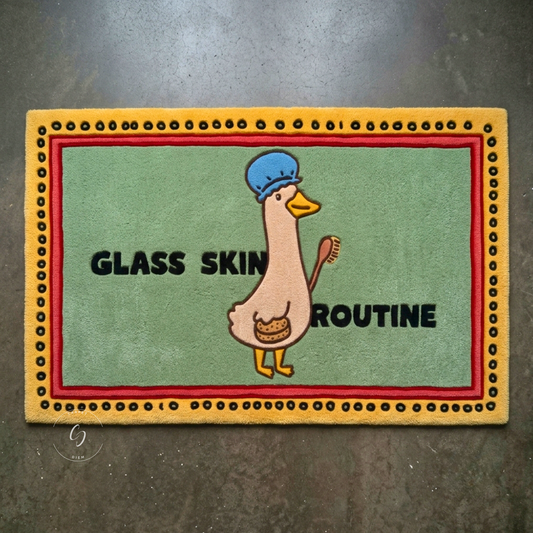 A rectangular decorative hand tufted bathroom entrance rug with a cartoon duck wearing a blue chef hat and holding a toothbrush, with the words 'GLASS SKIN ROUTINE' . 