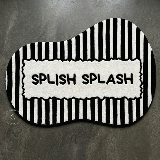 A black and white wavy hand tufted bathroom entrance rug with vertical stripes and a central white panel reading 'SPLISH SPLASH' in black letters.