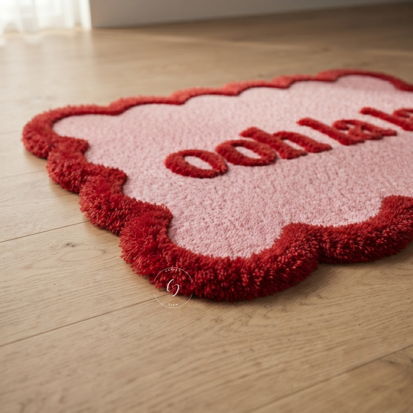 A pink and red cloud-shaped hand tufted bathroom entrance rug with the word 'ooh la la' in red, shown on a light wood floor.