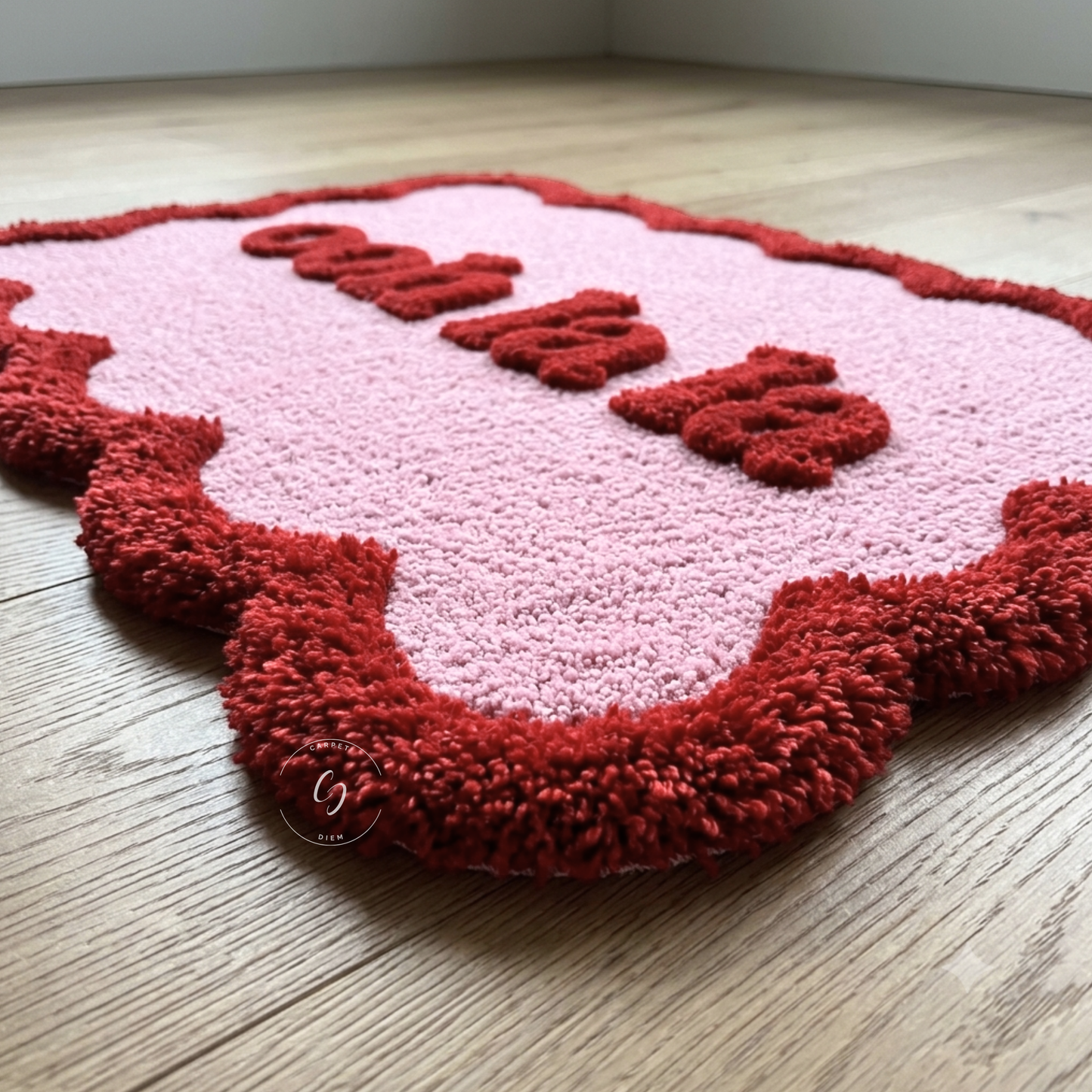 A pink and red shaggy hand tufted bathroom entrance rug with the word 'Ooh la la' raised in red letters, photographed on a light wood floor.