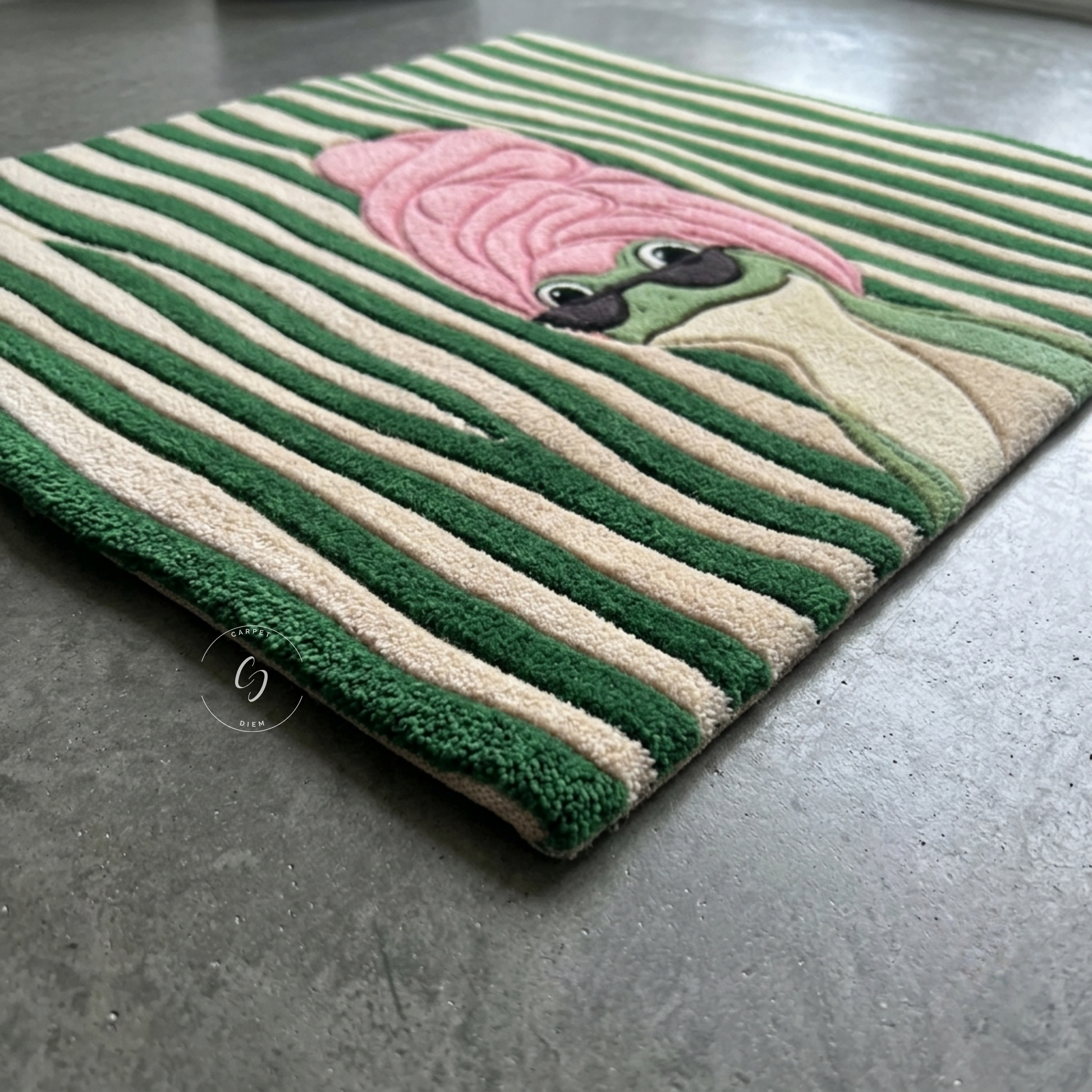 A rectangular hand tufted bathroom entrance rug with green and cream stripes and a cartoon frog character wearing pink towel, shown on a gray concrete floor.