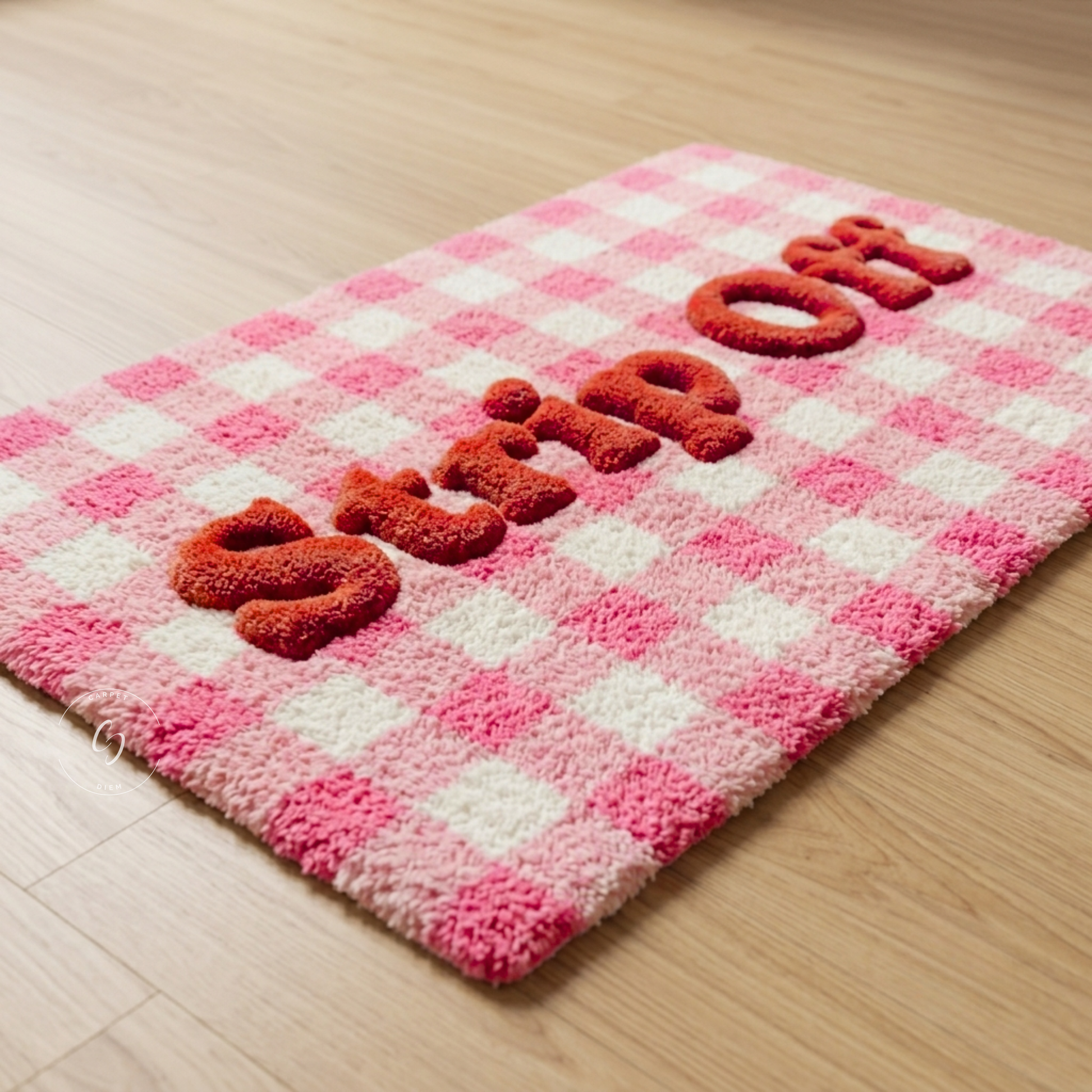 A pink and white checkered plush hand tufted bathroom entrance rug with raised red letters spelling 'STRIP ON' on a light wood floor.