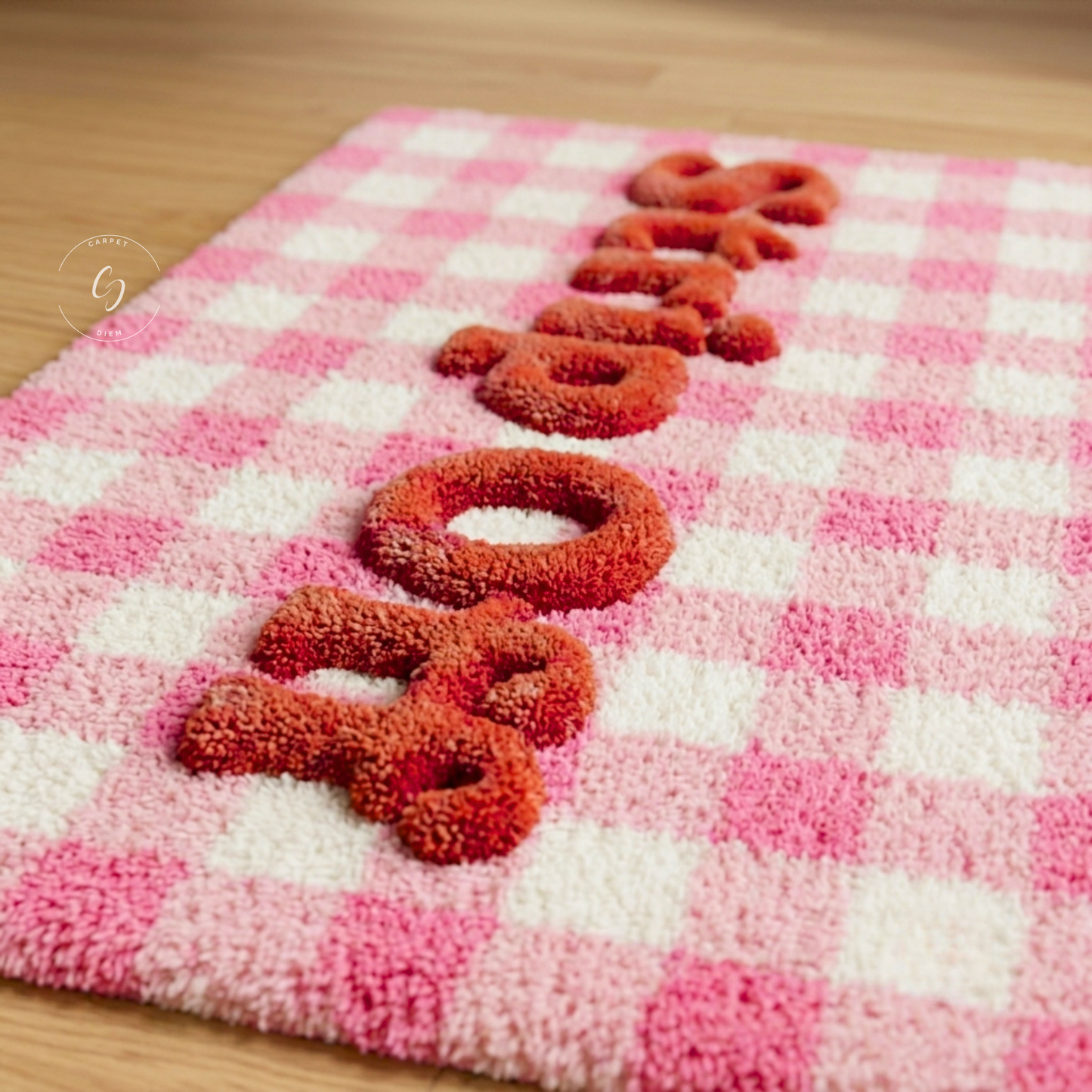 A pink and white checkered plush hand tufted bathroom entrance rug with raised red-orange lettering spelling 'strip off' on a light wood floor.