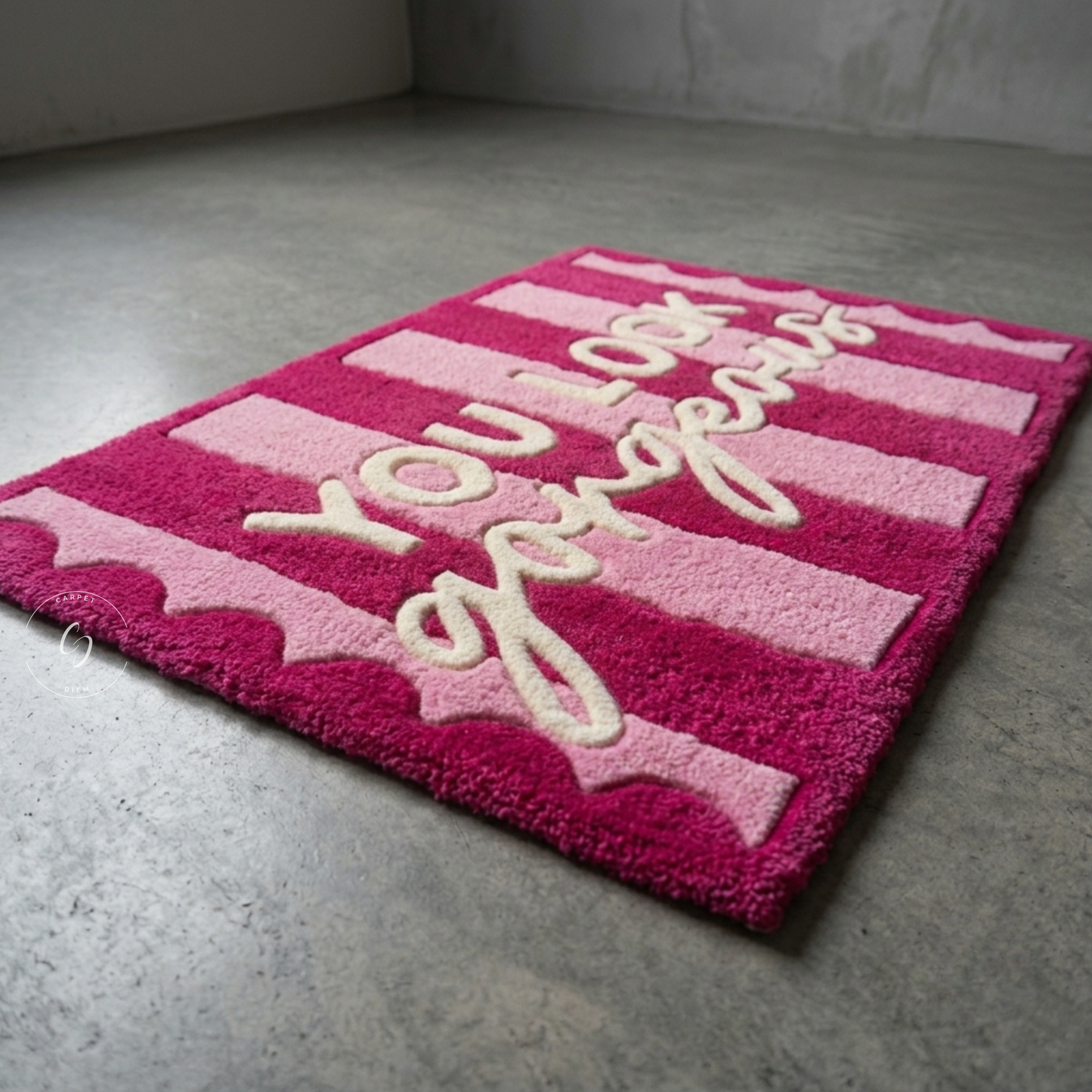 A rectangular pink and magenta striped hand tufted bathroom entrance rug with the phrase 'You Look Gorgeous' in cream cursive text, photographed on a grey concrete floor.