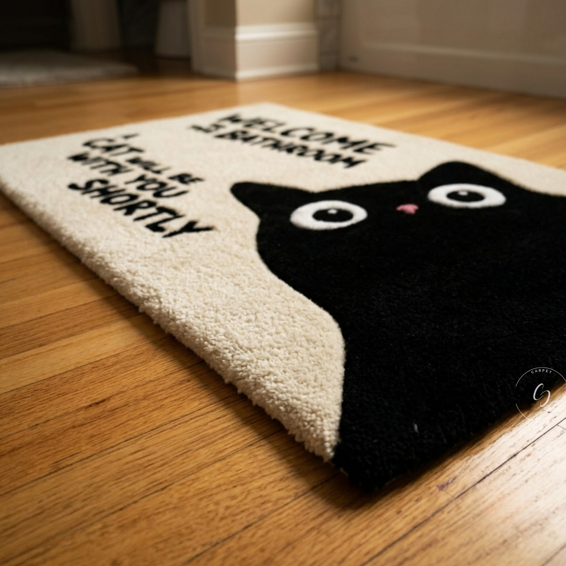 A rectangular hand tufted bathroom entrance rug with a black cat illustration and the text 'WELCOME TO BATHROOM CAT WILL BE WITH YOU SHORTLY' placed on a wooden floor.