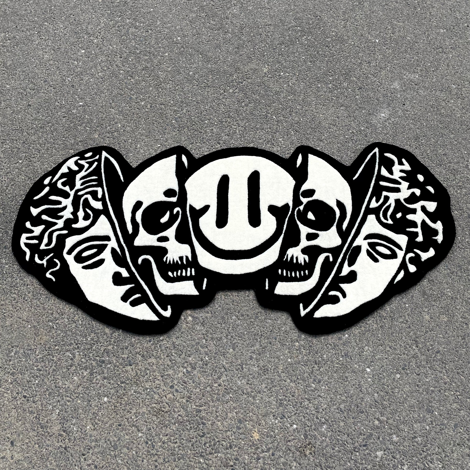 Black and white hand-tufted rug featuring classical Greek head, dual skulls, and smiley face in artistic street art style