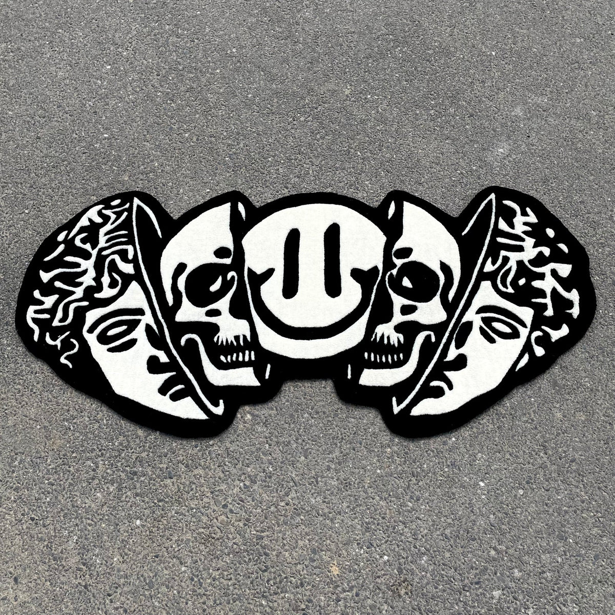 Black and white hand-tufted rug featuring classical Greek head, dual skulls, and smiley face in artistic street art style