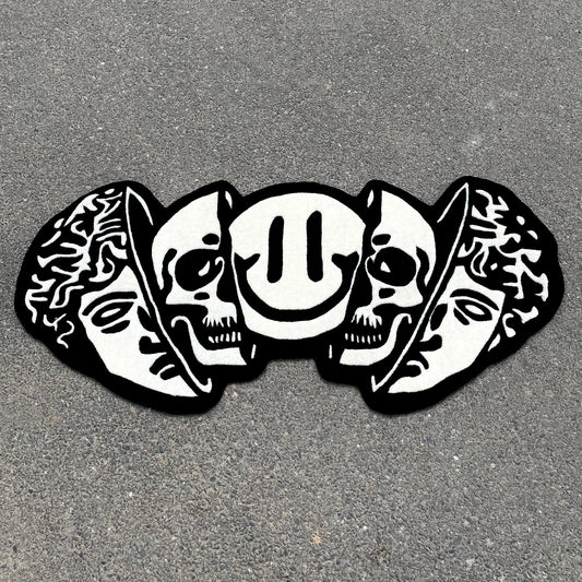 Black and white hand-tufted rug featuring classical Greek head, dual skulls, and smiley face in artistic street art style