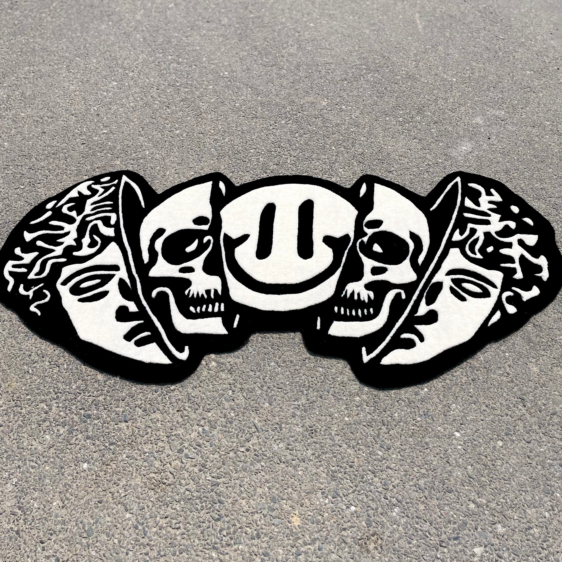 Monochromatic area rug displaying three heads design with Greek statue, skulls, and decorative elements in black and white